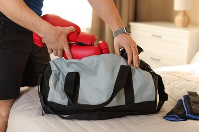 Photo of Man putting boxing gloves into gym bag indoors, closeup