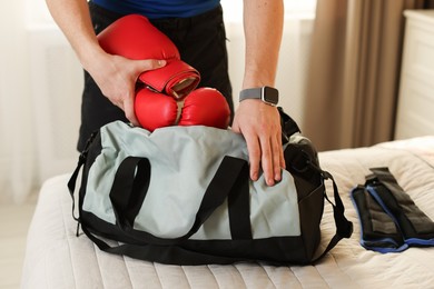 Man putting boxing gloves into gym bag indoors, closeup