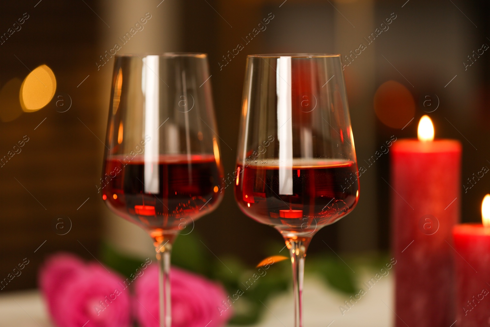 Photo of Glasses of red wine and burning candles against blurred background, closeup. Romantic dinner