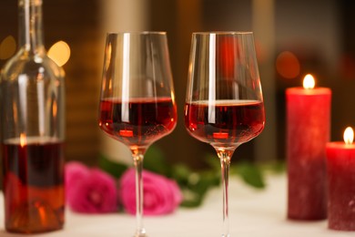 Photo of Glasses of red wine and burning candles against blurred background, closeup. Romantic dinner