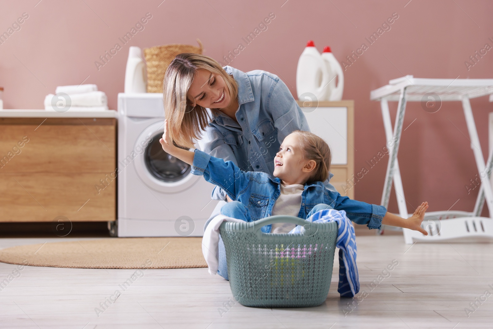 Photo of Mother and daughter having fun while doing laundry together at home