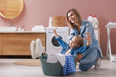 Mother and daughter having fun while doing laundry together at home