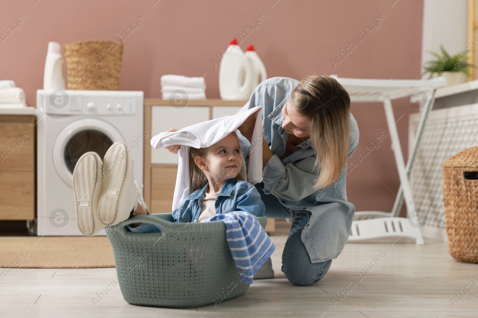 Photo of Little girl and her mom doing laundry together at home