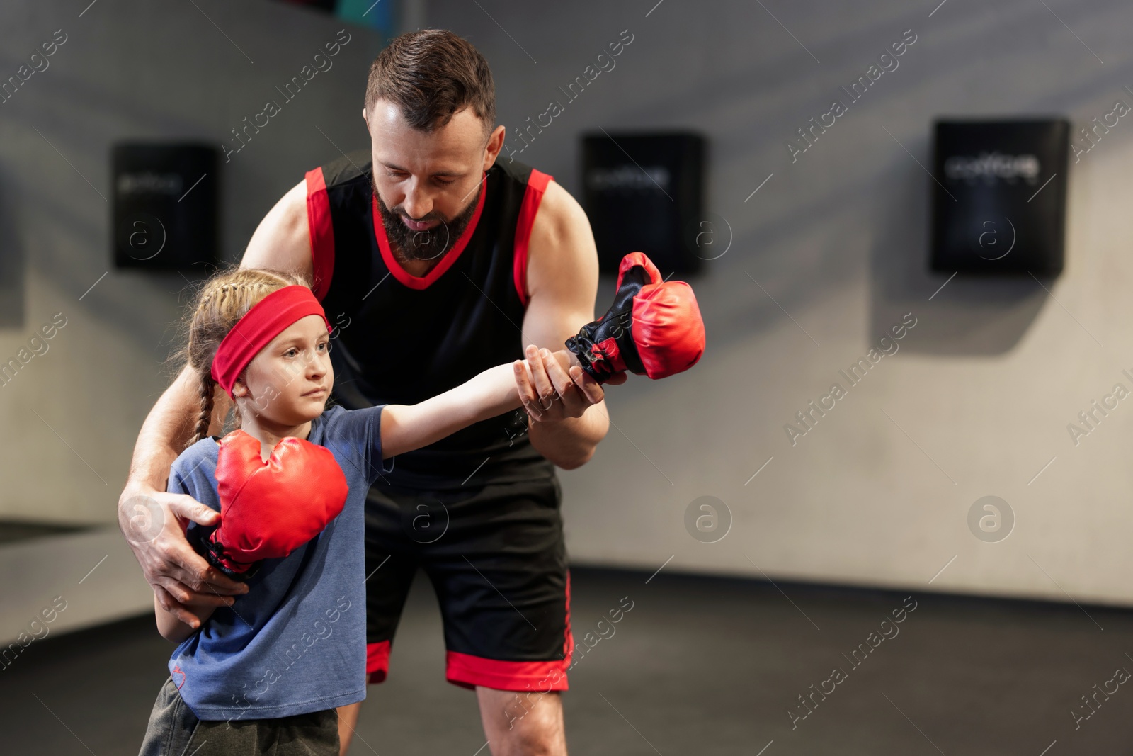 Photo of Girl in protective gloves having boxing practice with her coach at training center. Space for text