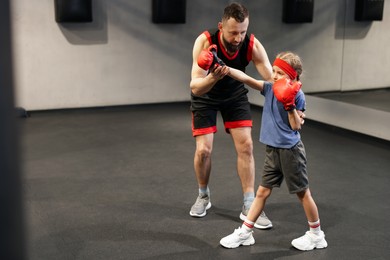 Photo of Girl in protective gloves having boxing practice with her coach at training center. Space for text