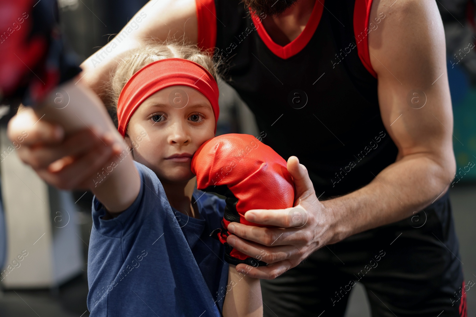 Photo of Girl in protective gloves having boxing practice with her coach at training center