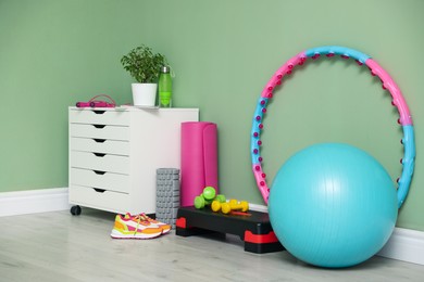 Different fitness equipment, sneakers and chest of drawers near green wall indoors