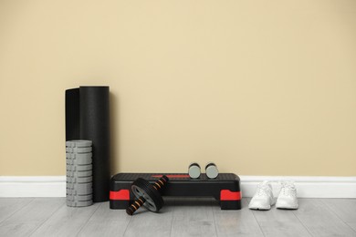 Photo of Different fitness equipment and sneakers near beige wall indoors