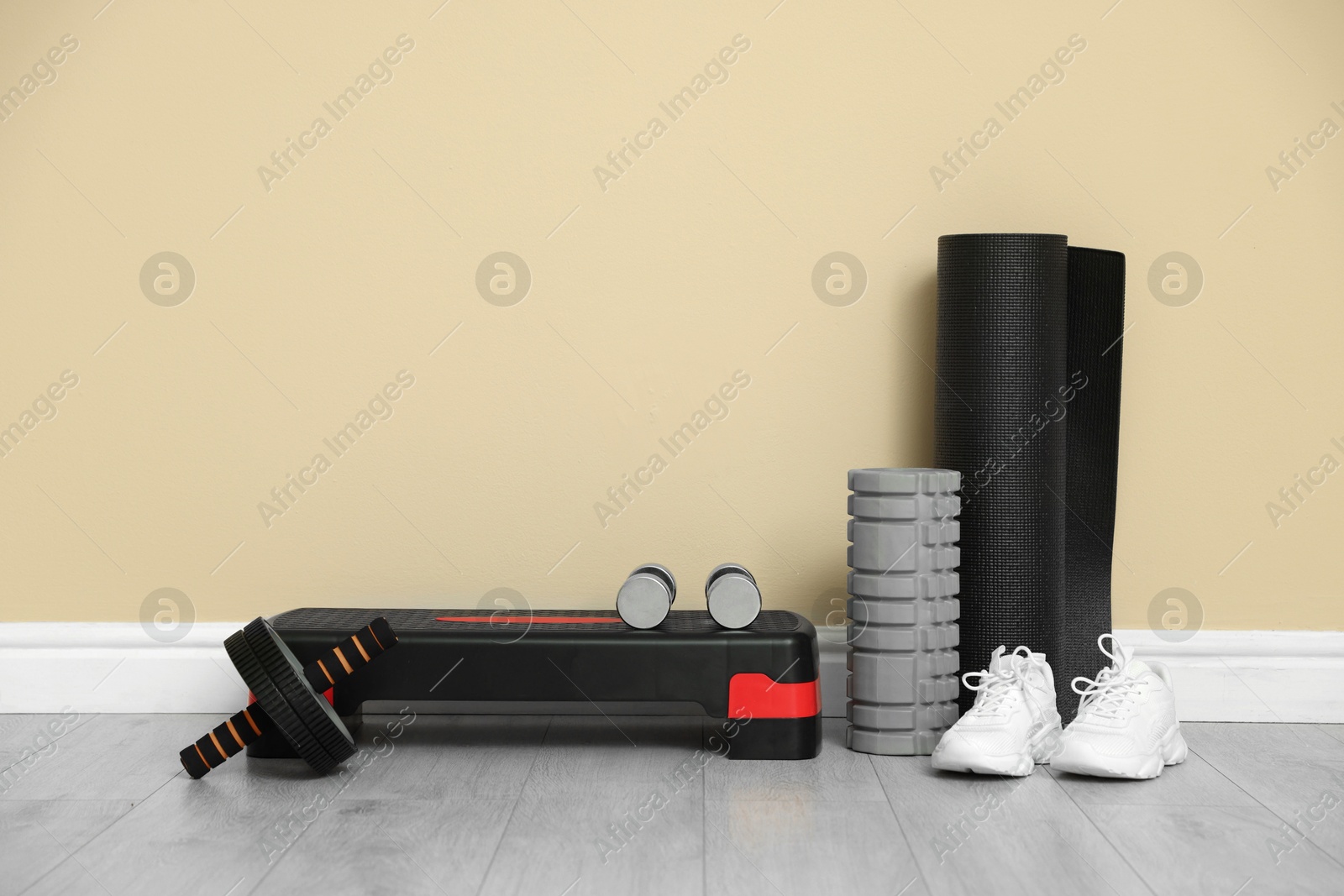 Photo of Different fitness equipment and sneakers near beige wall indoors