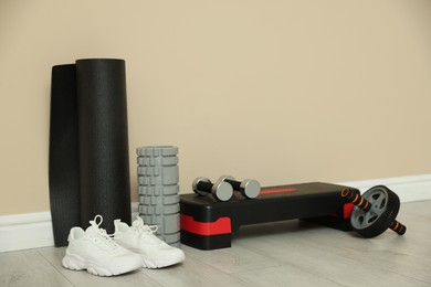 Photo of Different fitness equipment and sneakers near beige wall indoors