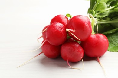 Photo of Bunch of fresh radishes on white wooden table, closeup