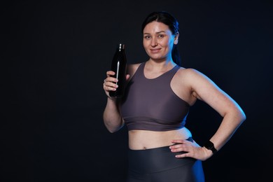 Photo of Plus size woman in gym clothes with water bottle on black background, space for text