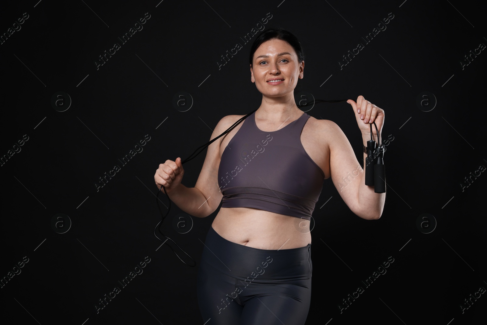 Photo of Plus size woman in gym clothes with skipping rope on black background