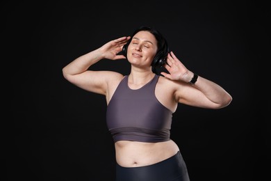 Photo of Plus size woman in gym clothes and headphones on black background