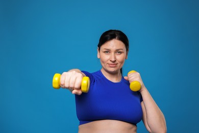 Photo of Plus size woman in gym clothes doing exercise with dumbbells on light blue background