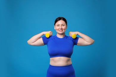 Photo of Plus size woman in gym clothes doing exercise with dumbbells on light blue background