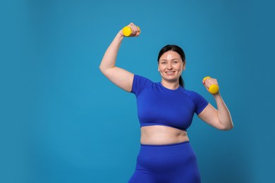 Photo of Plus size woman in gym clothes doing exercise with dumbbells on light blue background, space for text