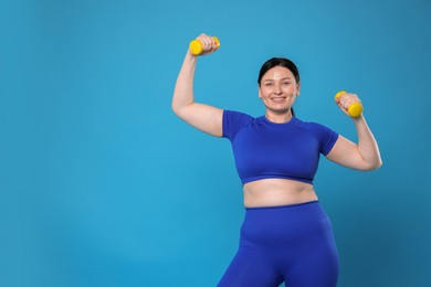 Photo of Plus size woman in gym clothes doing exercise with dumbbells on light blue background, space for text