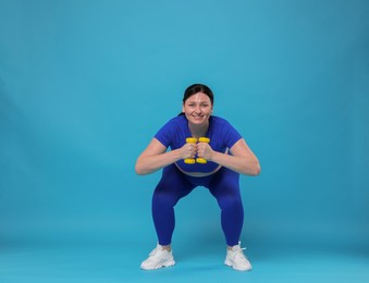 Photo of Plus size woman in gym clothes doing exercise with dumbbells on light blue background