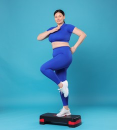 Photo of Plus size woman in gym clothes doing exercise with step platform on light blue background