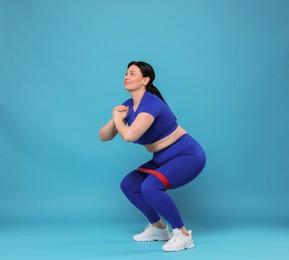 Photo of Plus size woman in gym clothes doing exercise with elastic band on light blue background