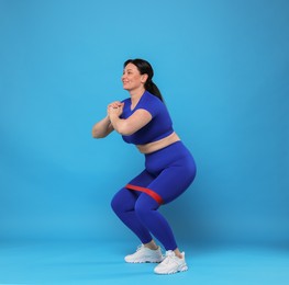 Photo of Plus size woman in gym clothes doing exercise with elastic band on light blue background