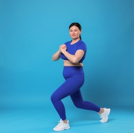 Photo of Plus size woman in gym clothes exercising on light blue background, space for text