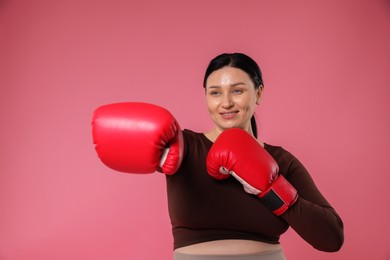 Plus size woman in gym clothes with boxing gloves on pink background