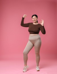 Plus size woman in gym clothes on pink background