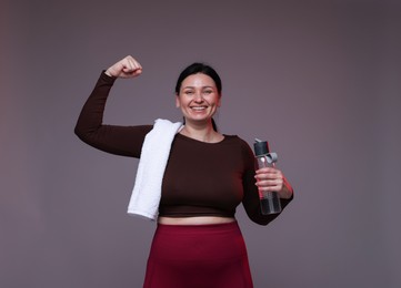 Photo of Plus size woman in gym clothes with water bottle and towel on grey background