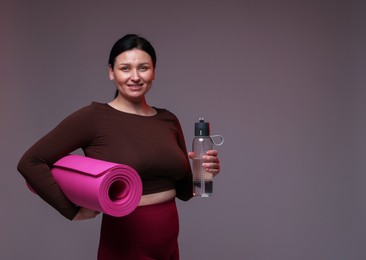 Photo of Plus size woman in gym clothes with water bottle and mat on grey background, space for text