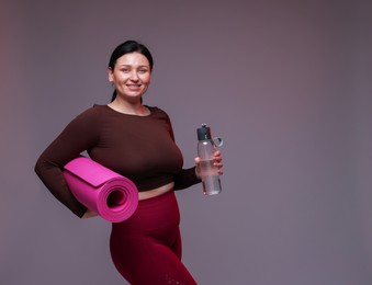 Photo of Plus size woman in gym clothes with water bottle and mat on grey background, space for text