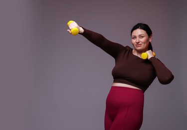 Photo of Plus size woman in gym clothes doing exercise with dumbbells on grey background, space for text