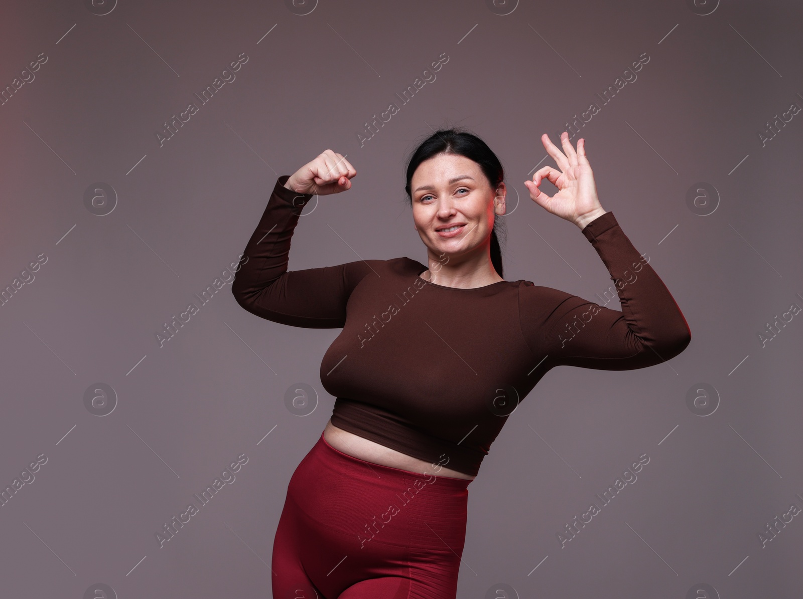 Photo of Plus size woman in gym clothes showing ok gesture on grey background