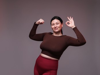 Plus size woman in gym clothes showing ok gesture on grey background