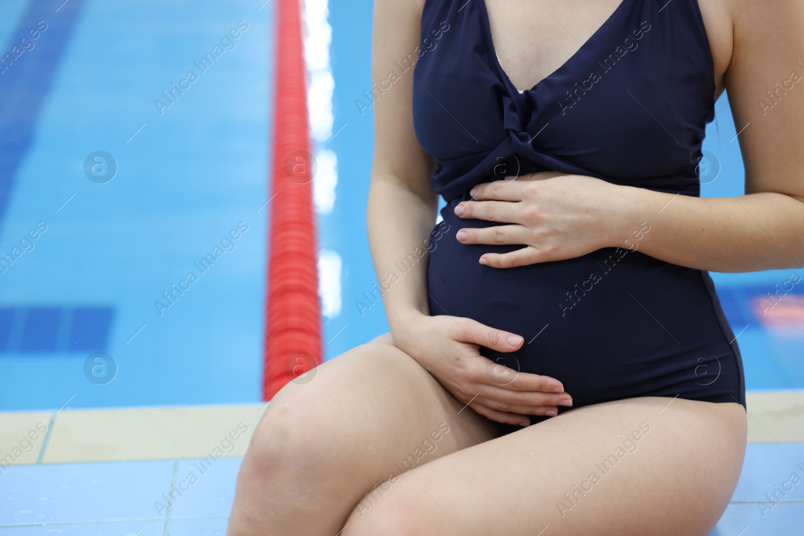 Photo of Pregnant woman sitting near swimming pool indoors, closeup. Space for text