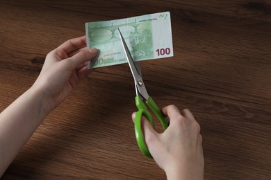 Photo of Woman cutting euro banknote at wooden table, closeup