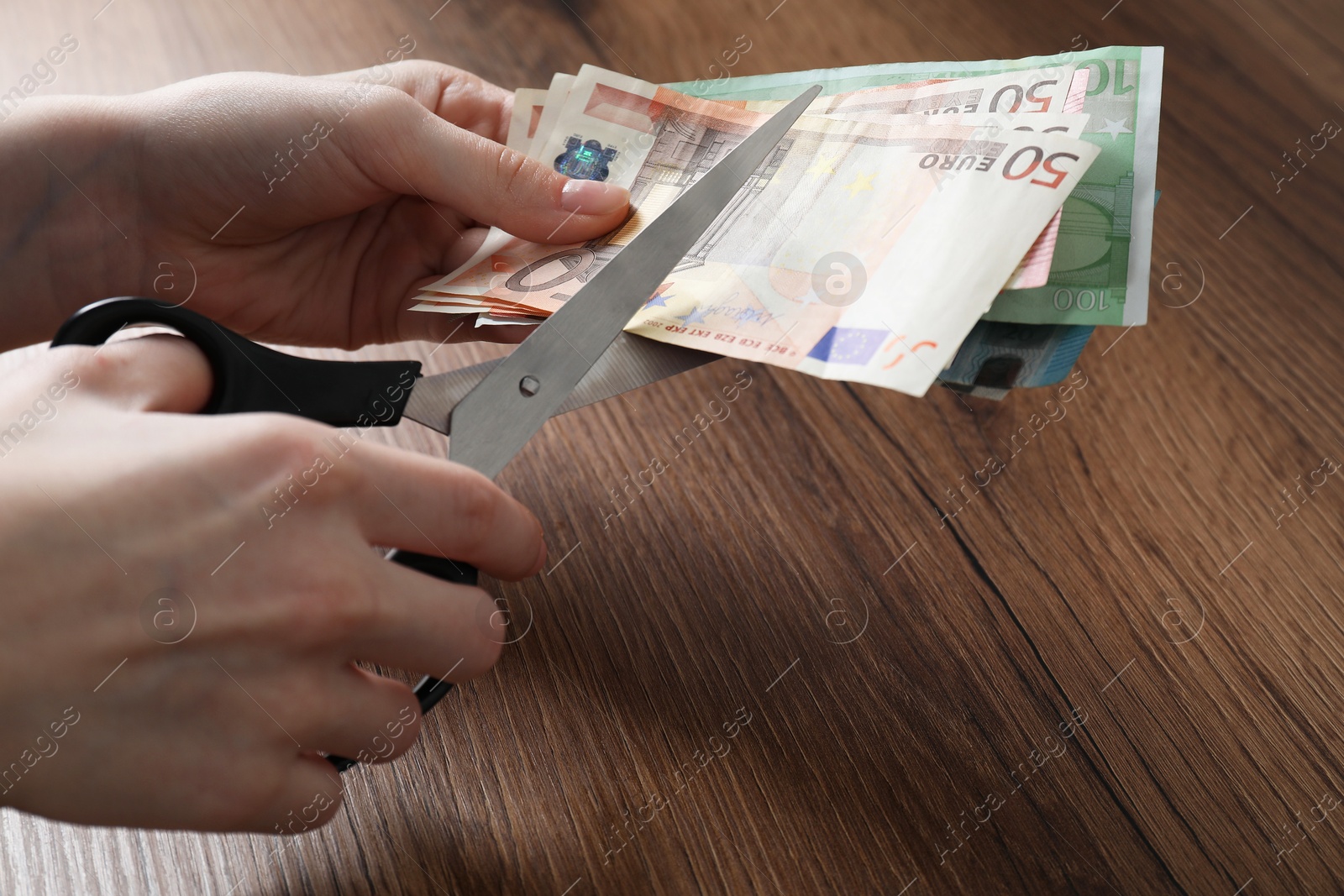 Photo of Woman cutting euro banknotes at wooden table, closeup