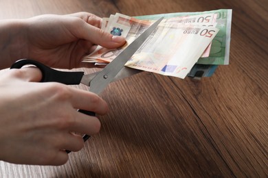 Woman cutting euro banknotes at wooden table, closeup