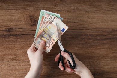 Woman cutting euro banknotes at wooden table, top view