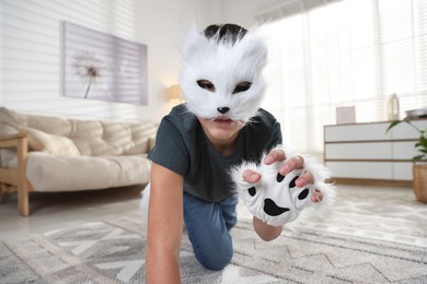 Photo of Quadrobics. Boy wearing cat mask and gloves on floor at home