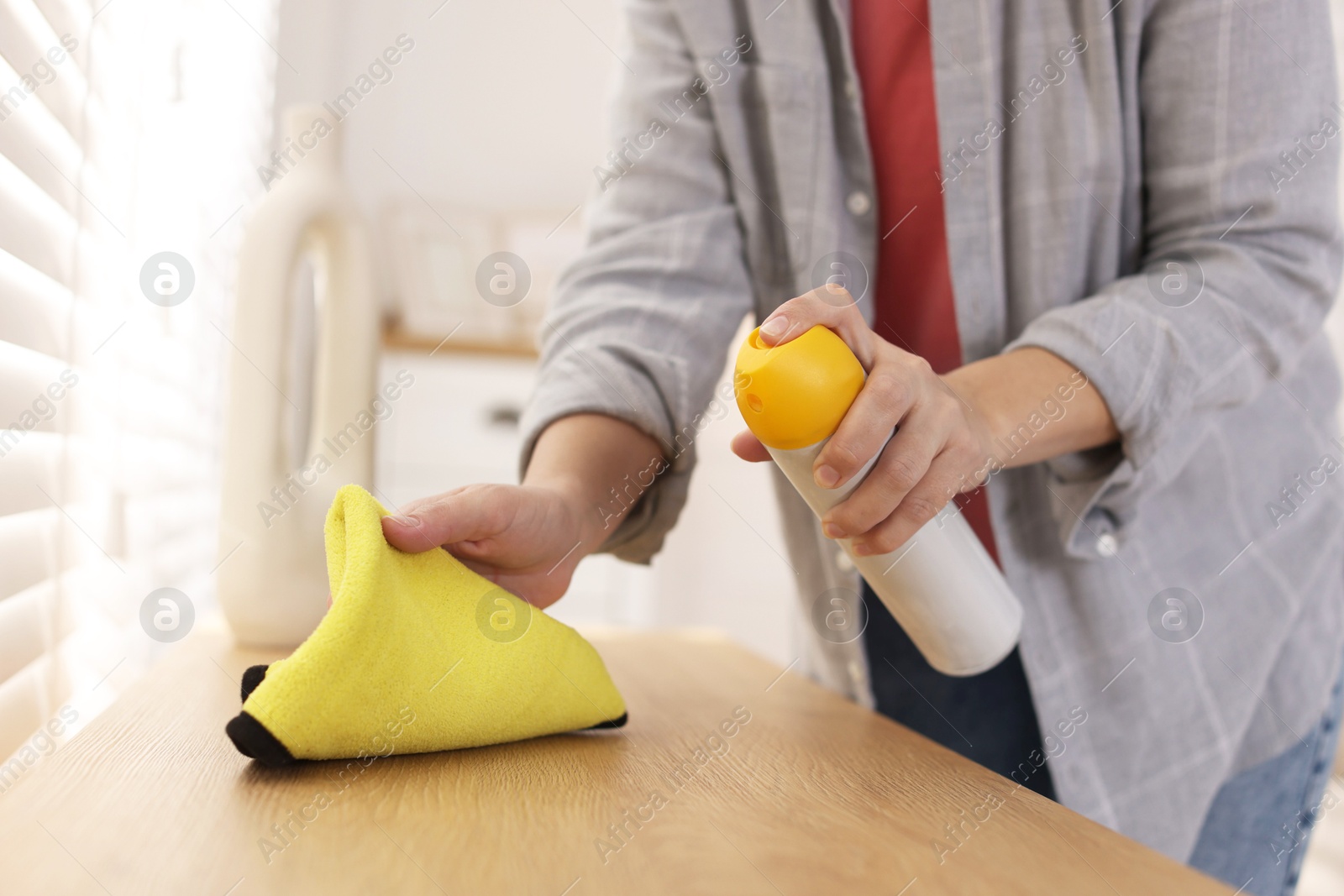 Photo of Woman using cleaning product while polishing wooden table with rag indoors, closeup