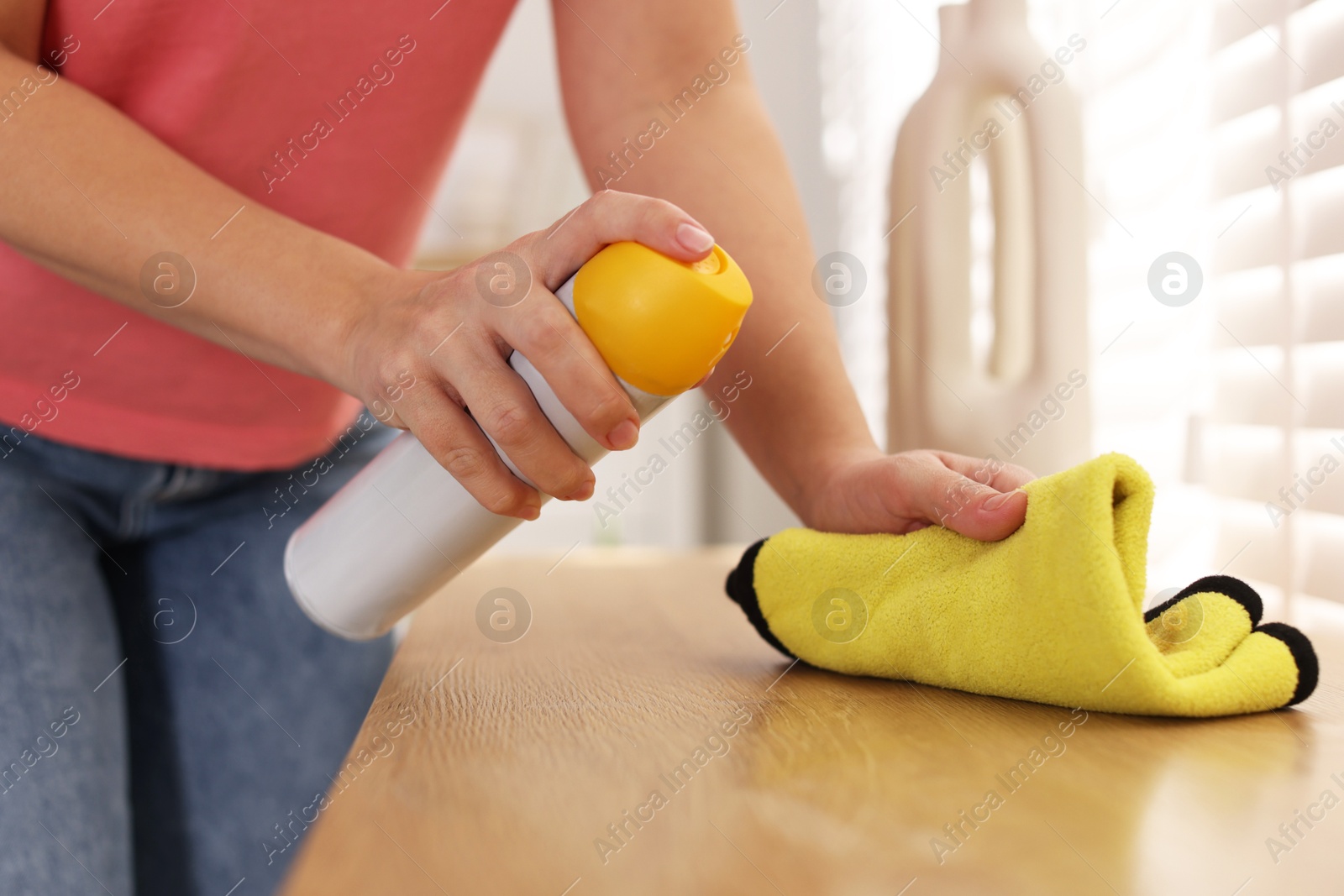 Photo of Woman using cleaning product while polishing wooden table with rag indoors, closeup