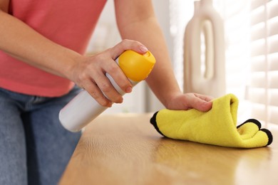 Woman using cleaning product while polishing wooden table with rag indoors, closeup