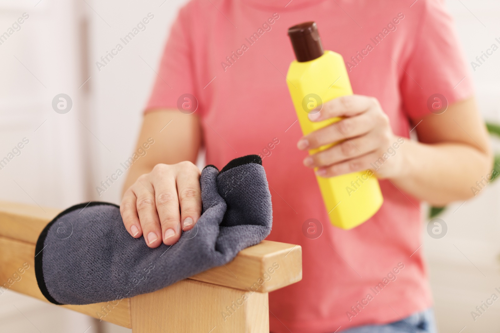 Photo of Woman with cleaning product and rag polishing wooden armrest at home, closeup