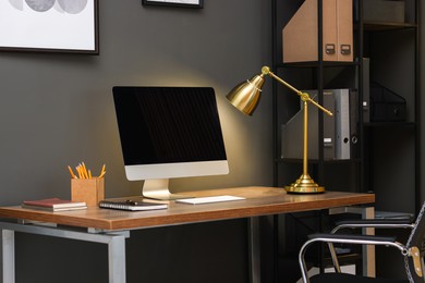 Photo of Comfortable workplace with computer and lamp on wooden desk in home office