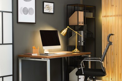 Photo of Comfortable workplace with computer and lamp on wooden desk in home office