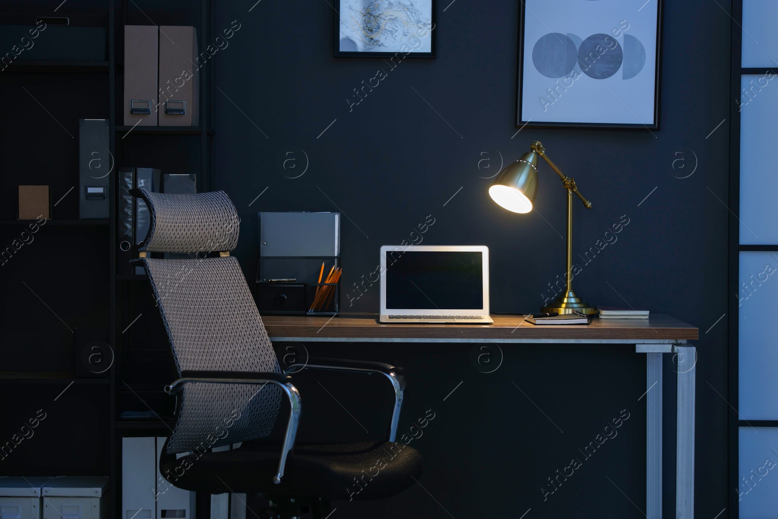 Comfortable workplace with laptop and lamp on wooden desk at home office in evening Photo of Comfortable workplace with laptop and lamp on wooden desk at home office in evening