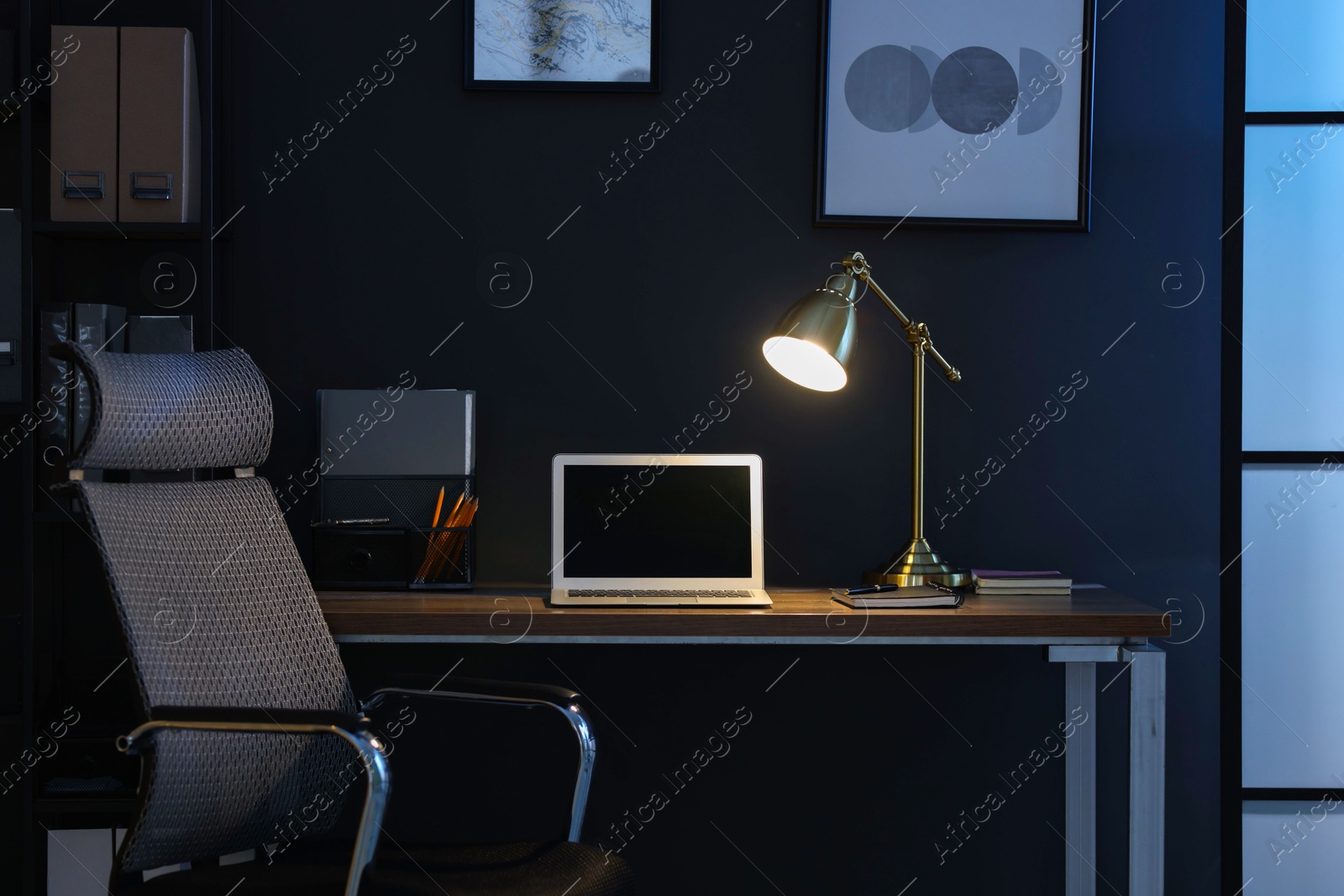 Comfortable workplace with laptop and lamp on wooden desk at home office in evening Photo of Comfortable workplace with laptop and lamp on wooden desk at home office in evening