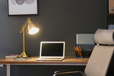 Photo of Home office. Comfortable workplace with laptop and lamp on wooden desk in room